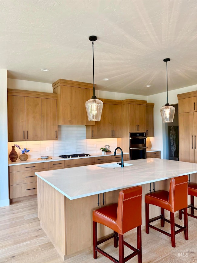 Kitchen with a large island, backsplash, a breakfast bar area, and light wood finished floors