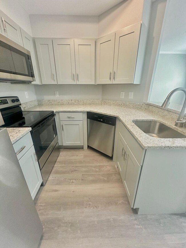 Kitchen with stainless steel appliances, light stone counters, light wood-style flooring, white cabinets, and a peninsula