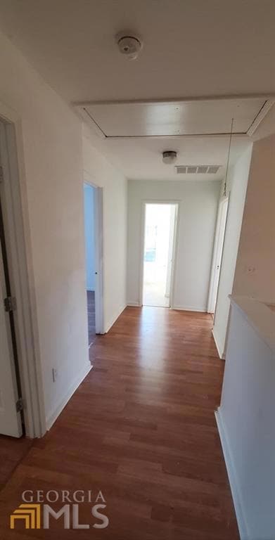 Hall with attic access, wood finished floors, and baseboards