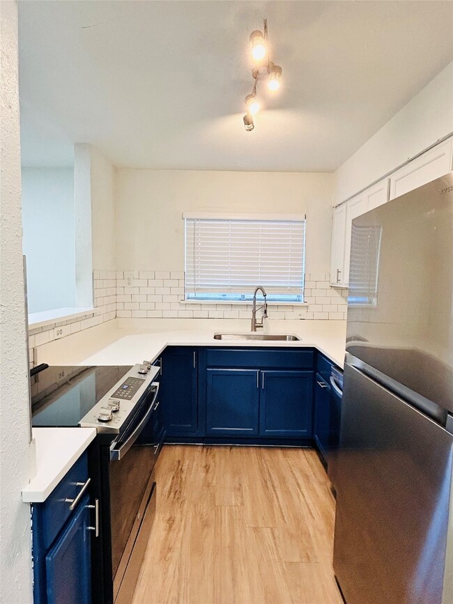 Kitchen featuring blue cabinetry, freestanding refrigerator, range with electric stovetop, light wood-style floors, and tasteful backsplash