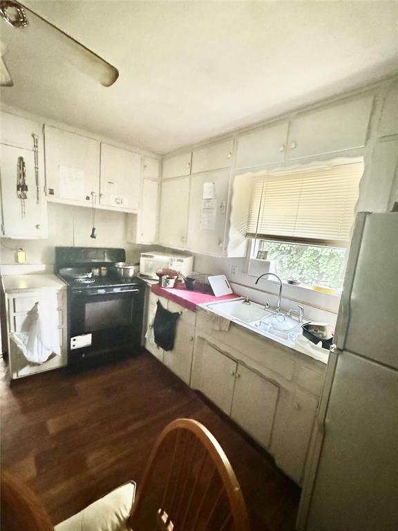 Kitchen featuring freestanding refrigerator, black stove, light countertops, dark wood finished floors, and a sink