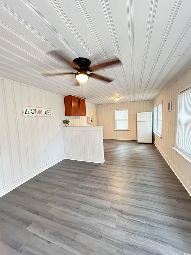Unfurnished living room with ceiling fan, dark wood finished floors, and wooden walls