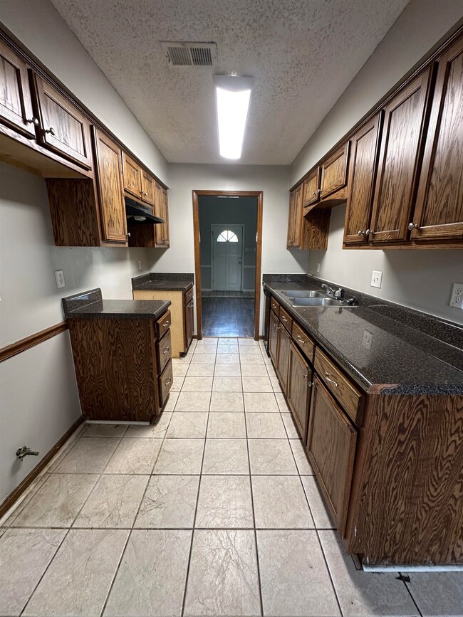 Kitchen featuring a textured ceiling, dark brown cabinets, under cabinet range hood, dark stone countertops, and light tile patterned floors