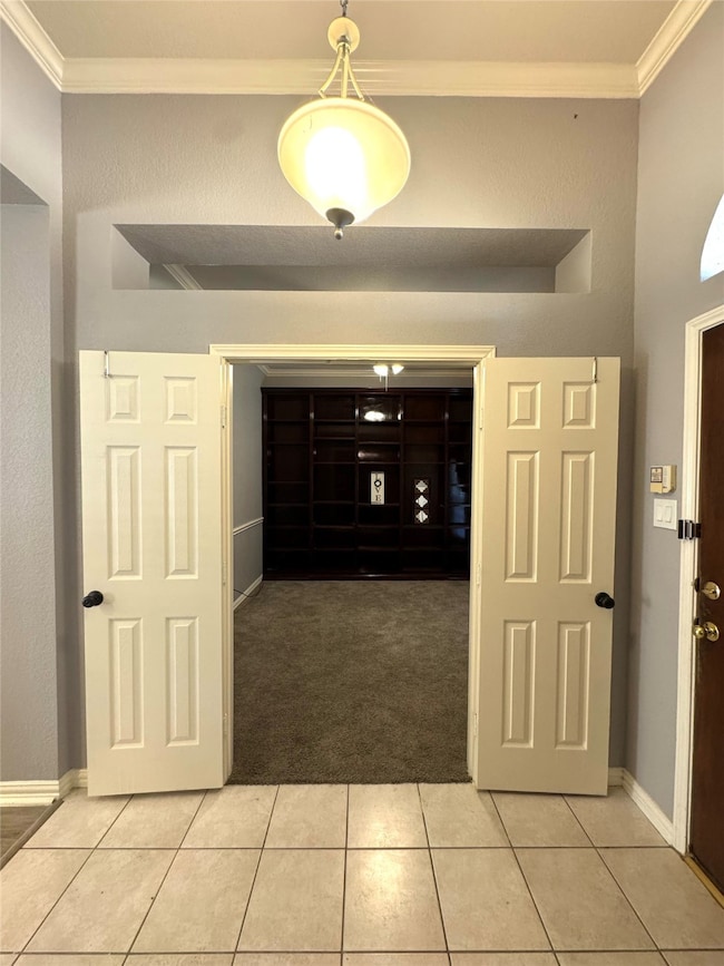 Foyer entrance featuring ornamental molding, light tile patterned floors, a textured wall, and light colored carpet