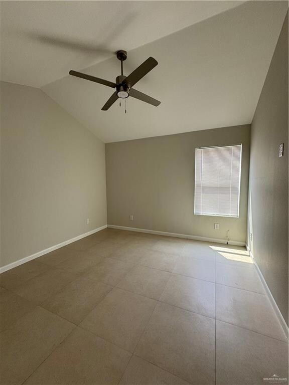 Tiled spare room with vaulted ceiling, baseboards, and ceiling fan