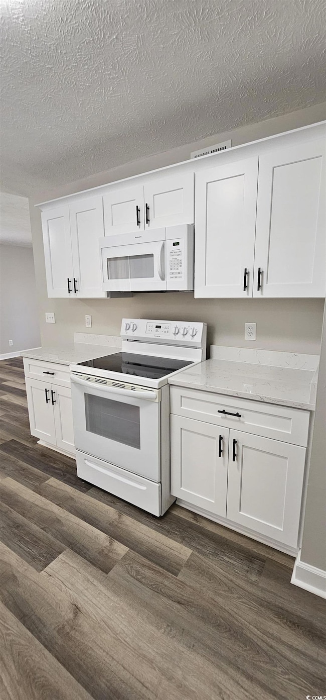 Kitchen with white appliances, white cabinets, dark wood-style flooring, a textured ceiling, and light stone countertops