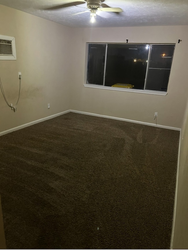 Bedroom with carpet, a textured ceiling, ceiling fan, and an AC wall unit