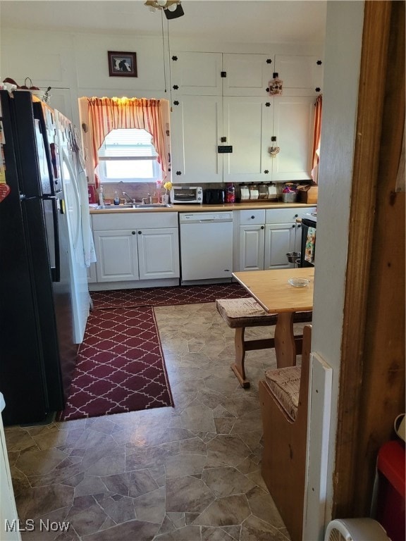 Kitchen with white cabinets, refrigerator, dishwasher, dark stone finish flooring, and light countertops