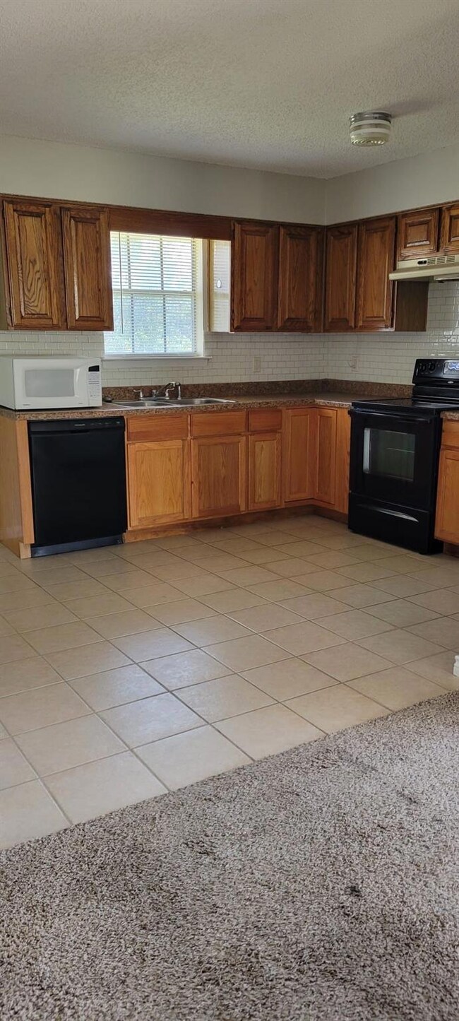 Kitchen with light tile patterned flooring, black appliances, decorative backsplash, and a textured ceiling