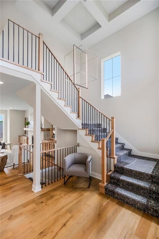 Stairs featuring hardwood / wood-style flooring, plenty of natural light, coffered ceiling, beamed ceiling, and a towering ceiling