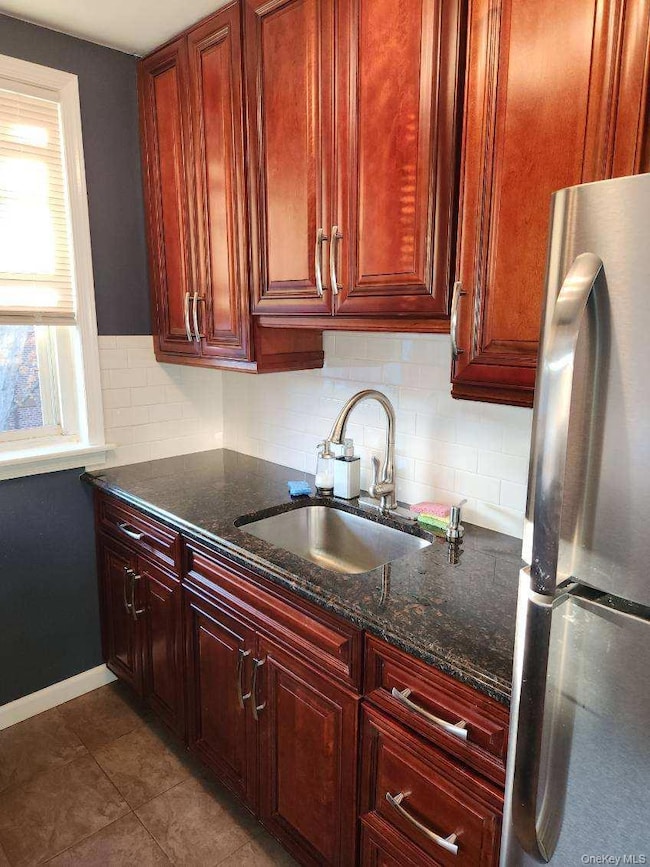 Kitchen featuring decorative backsplash, freestanding refrigerator, dark stone countertops, and dark brown cabinets