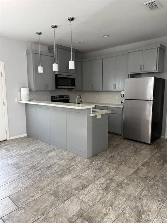 Kitchen featuring gray cabinetry, stainless steel appliances, a peninsula, light countertops, and decorative light fixtures