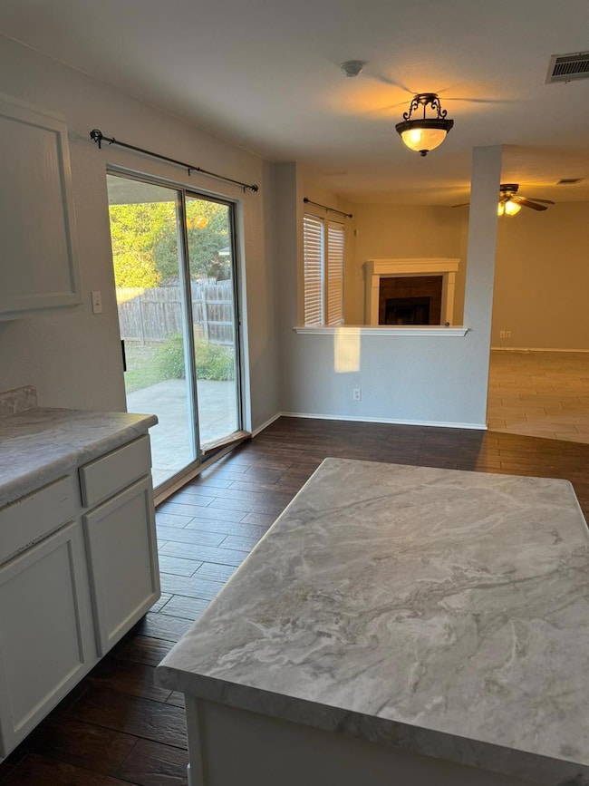 Unfurnished dining area with dark wood-style floors, ceiling fan, and a fireplace