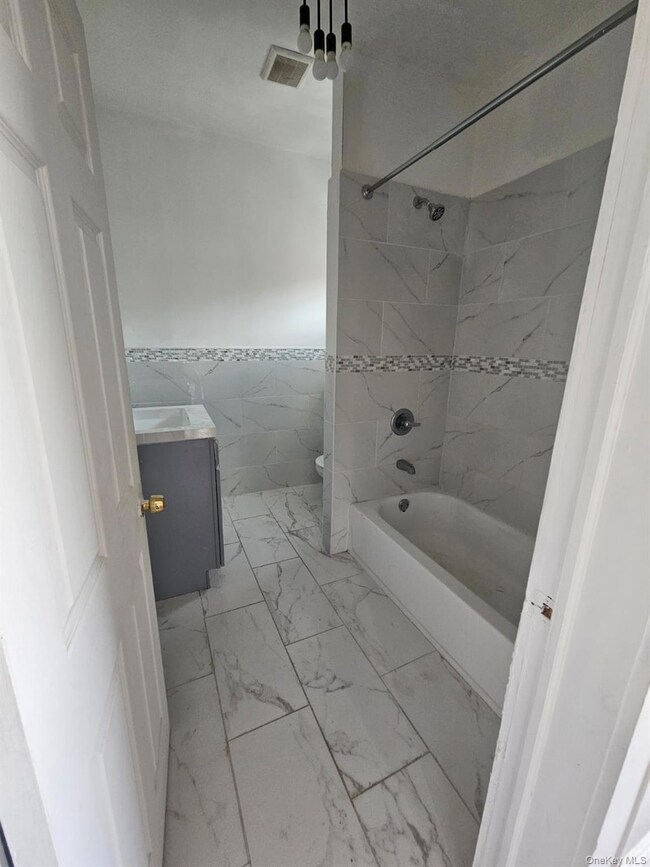 Bathroom featuring tile walls, vanity, wainscoting, bathing tub / shower combination, and light marble finish flooring