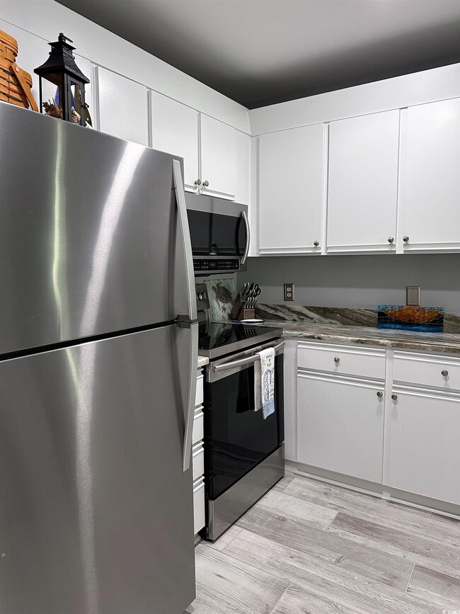 Kitchen with stainless steel appliances, white cabinetry, light wood finished floors, and dark stone counters