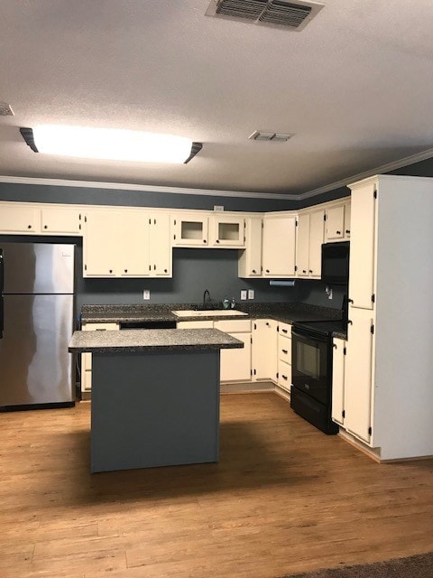 Kitchen with dark countertops, freestanding refrigerator, a kitchen island, black range with electric stovetop, and dark wood finished floors