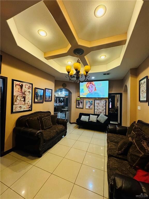 Living room featuring a chandelier, coffered ceiling, light tile floors, and a raised ceiling