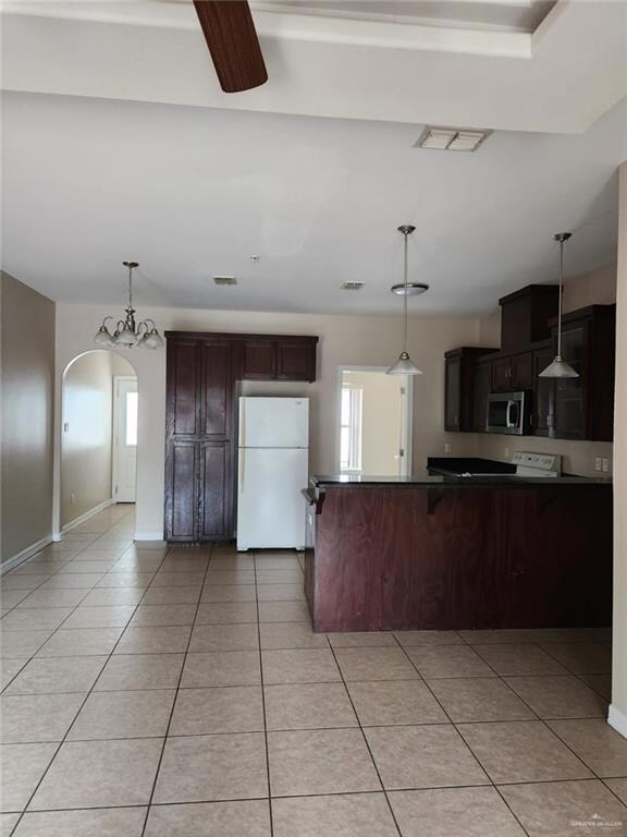 Kitchen featuring white refrigerator, hanging light fixtures, light tile floors, and kitchen peninsula