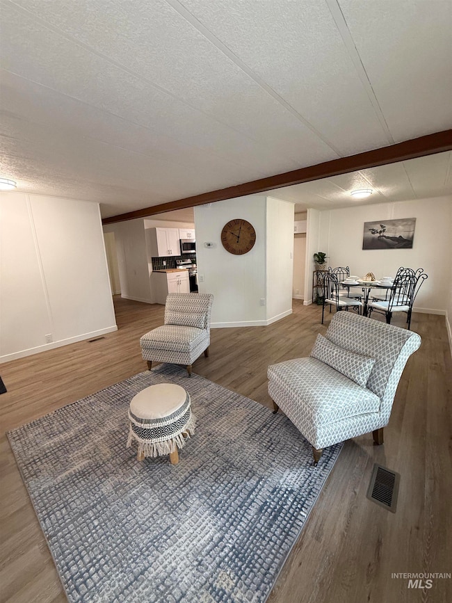 Living room with a textured ceiling, wood finished floors, and beamed ceiling