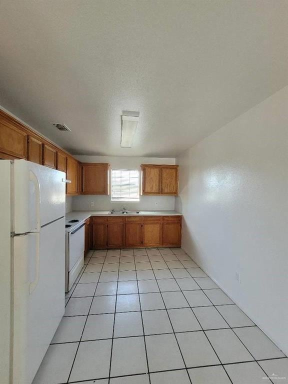Kitchen featuring sink, white appliances, a textured ceiling, and light tile patterned flooring