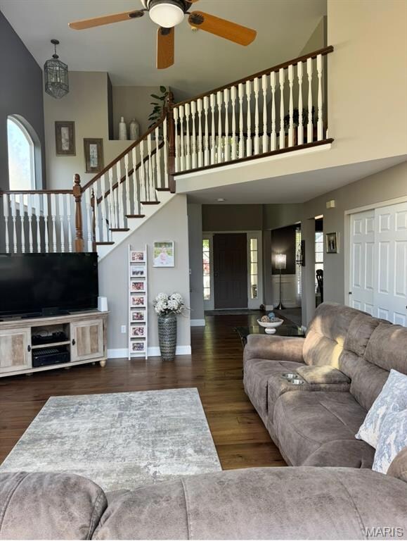 Living area featuring a high ceiling, a ceiling fan, wood finished floors, and stairs