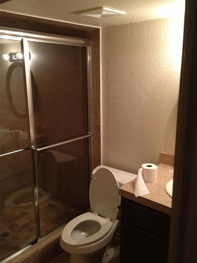 Bathroom with a textured wall, vanity, a stall shower, and a textured ceiling