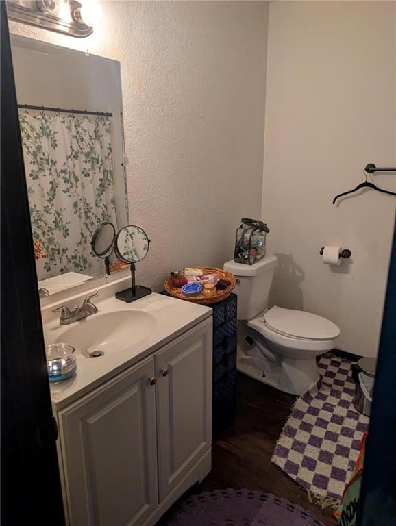 Full bathroom featuring a textured wall, vanity, a shower with shower curtain, and dark wood-type flooring