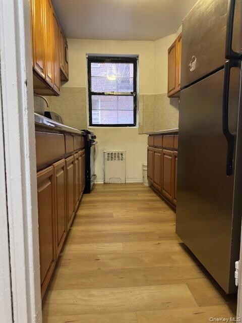 Kitchen with dark countertops, freestanding refrigerator, tile walls, brown cabinetry, and light wood-type flooring