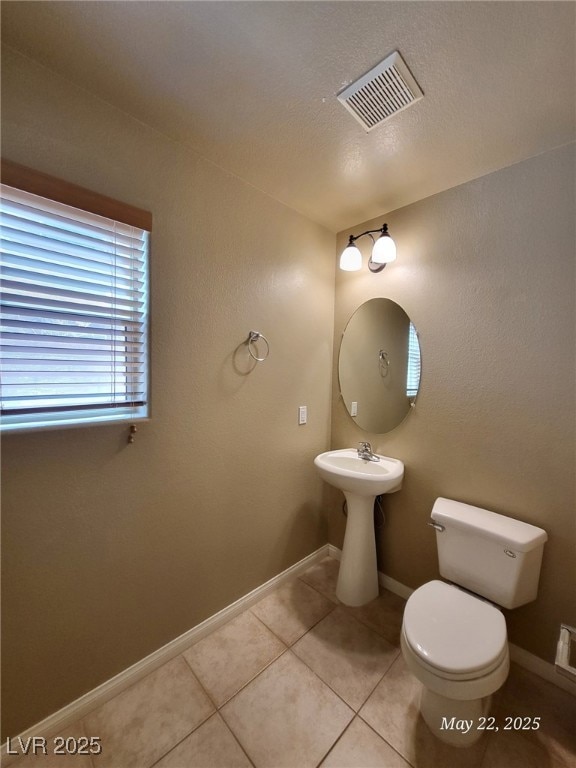 Half bathroom with toilet, tile patterned floors,
