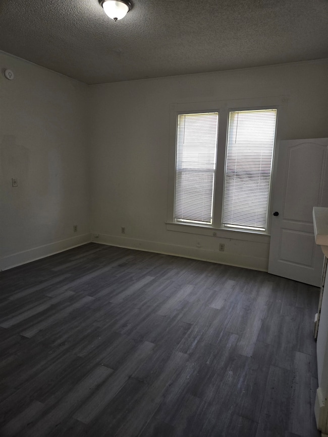 Unfurnished room featuring dark wood-type flooring, a textured ceiling, and baseboards