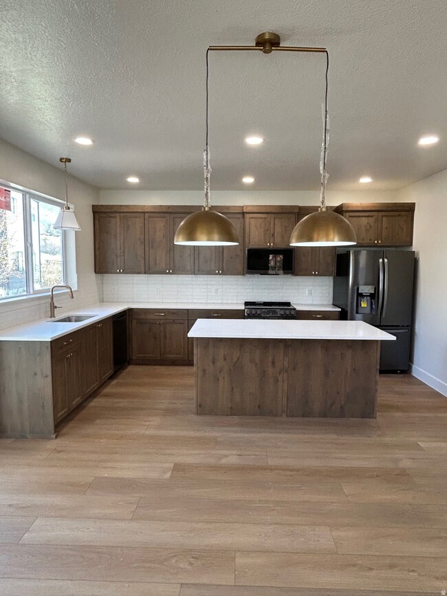 Kitchen with decorative light fixtures, black appliances, backsplash, a center island, and a textured ceiling
