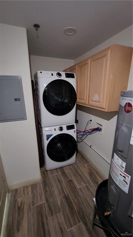 Laundry room with stacked washing machine and dryer, cabinet space, electric panel, water heater, and dark wood-type flooring