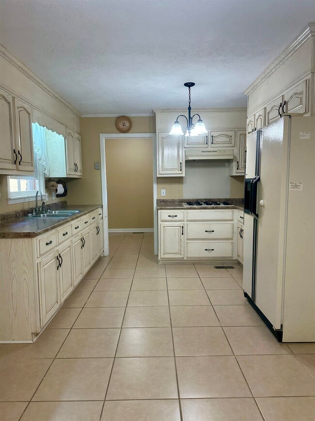 Kitchen with dark countertops, white refrigerator with ice dispenser, pendant lighting, ornamental molding, and light tile patterned floors