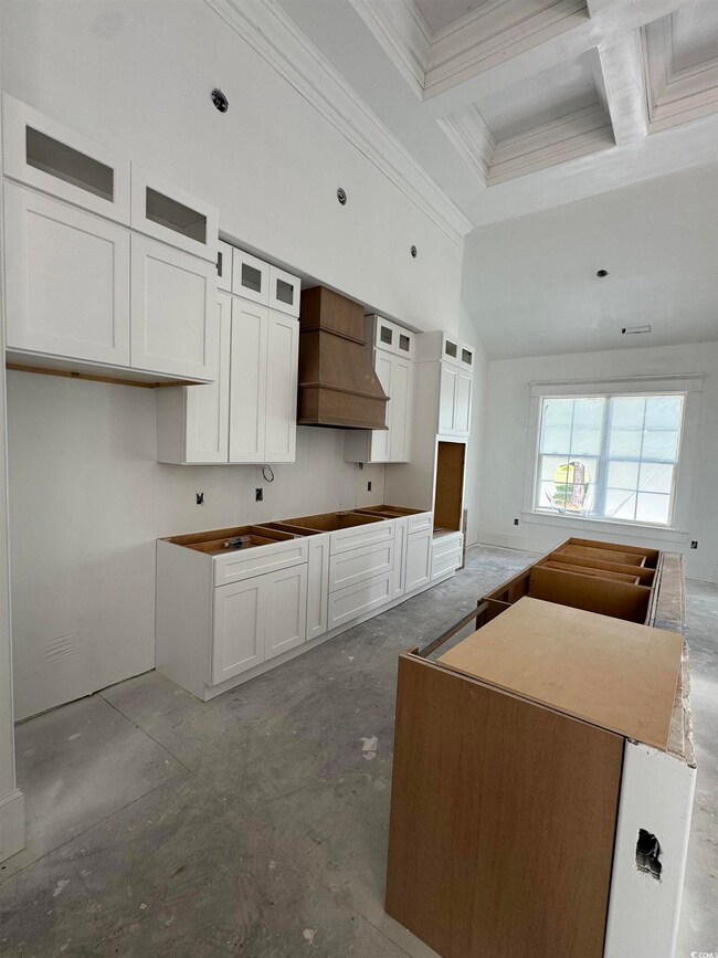Kitchen featuring crown molding, custom exhaust hood, coffered ceiling, glass insert cabinets, and white cabinetry