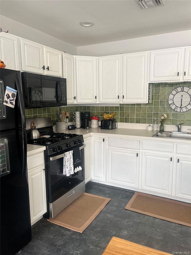 Kitchen featuring white cabinets, black appliances, decorative backsplash, and light countertops