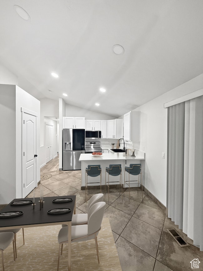 Kitchen featuring light countertops, vaulted ceiling, a breakfast bar area, a peninsula, and white cabinetry