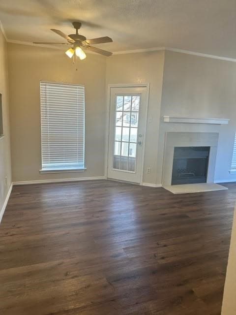 Unfurnished living room featuring crown molding, dark wood finished floors, ceiling fan, and a fireplace