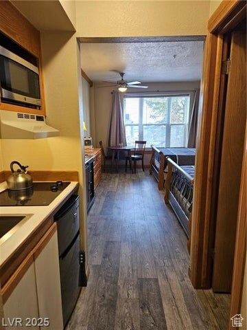 Kitchen with exhaust hood, stainless steel microwave, dark wood-type flooring, ceiling fan, and light countertops