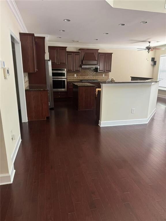 Kitchen featuring custom range hood, a center island, dark countertops, dark wood-style flooring, and appliances with stainless steel finishes
