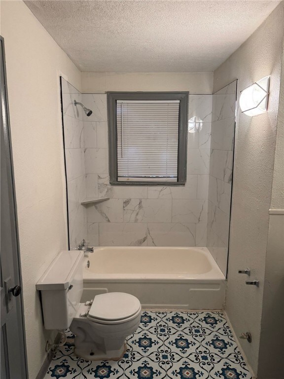 Bathroom featuring tiled shower / bath, toilet, ti