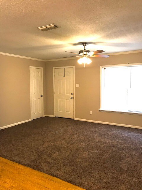 Carpeted spare room featuring a textured ceiling, crown molding, wood finished floors, and ceiling fan