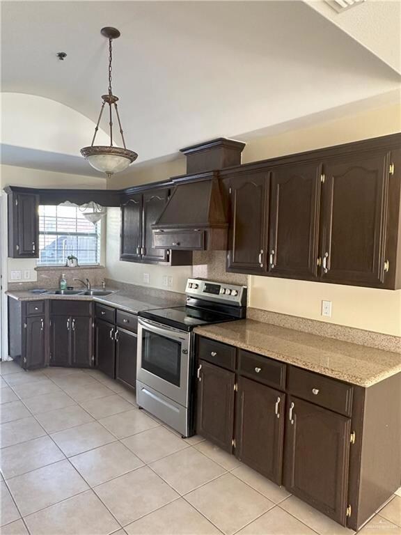 Kitchen featuring electric stove, vaulted ceiling, custom range hood, decorative light fixtures, and dark brown cabinets