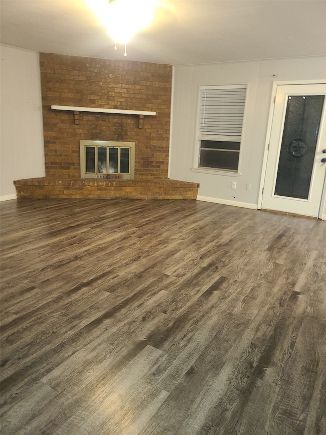 Unfurnished living room featuring dark wood-type flooring, a brick fireplace, and a ceiling fan