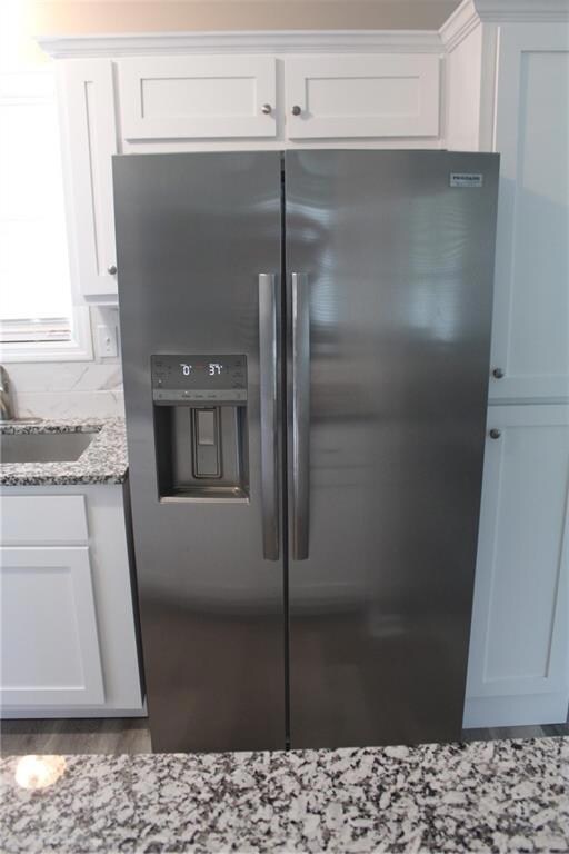 Kitchen featuring stainless steel fridge, a sink, white cabinets, light stone countertops, and wood finished floors