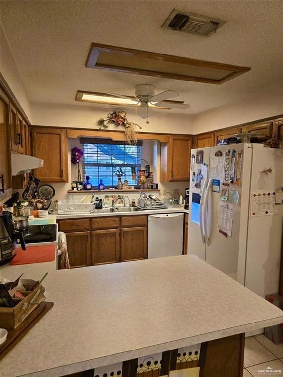 Kitchen featuring white fridge with ice dispenser, brown cabinets, light countertops, a peninsula, and a textured ceiling