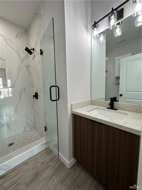 Bathroom with wood-type flooring, a shower with door, and vanity