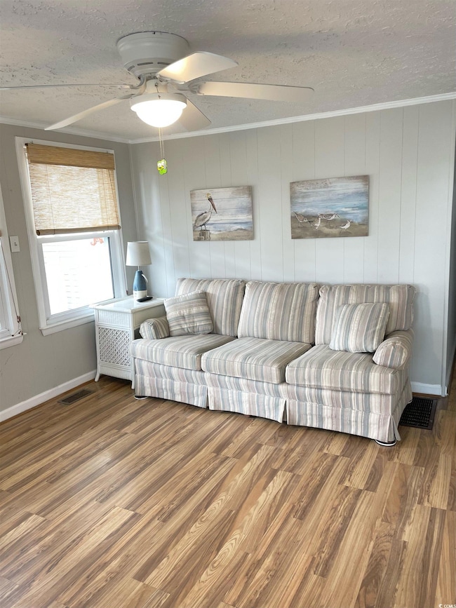 Living room with a ceiling fan, wood finished floors, a textured ceiling, and crown molding
