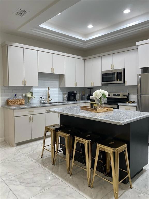 Kitchen with a kitchen breakfast bar, white cabinetry, stainless steel appliances, a kitchen island, and backsplash
