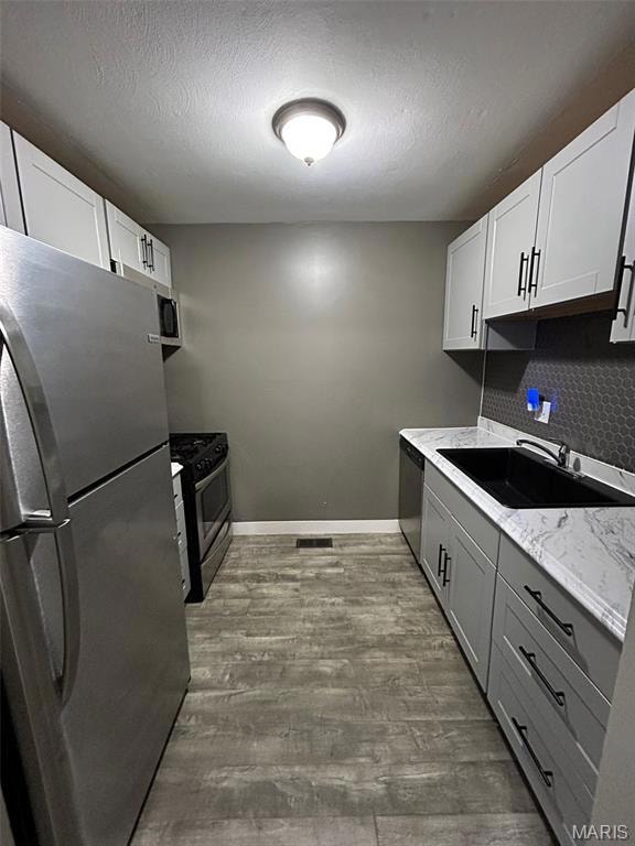 Kitchen with appliances with stainless steel finishes, decorative backsplash, a textured ceiling, gray cabinetry, and light wood-style flooring