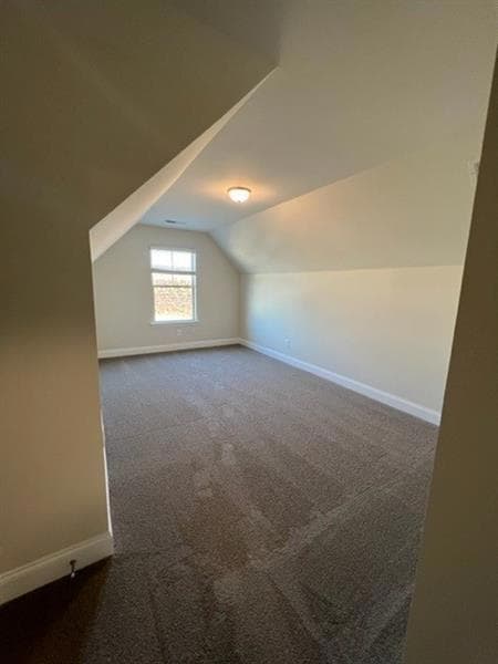 Additional living space featuring vaulted ceiling, baseboards, and dark colored carpet